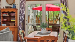 A dining area with a table, chairs, a vase with flowers, and a window with a red umbrella.