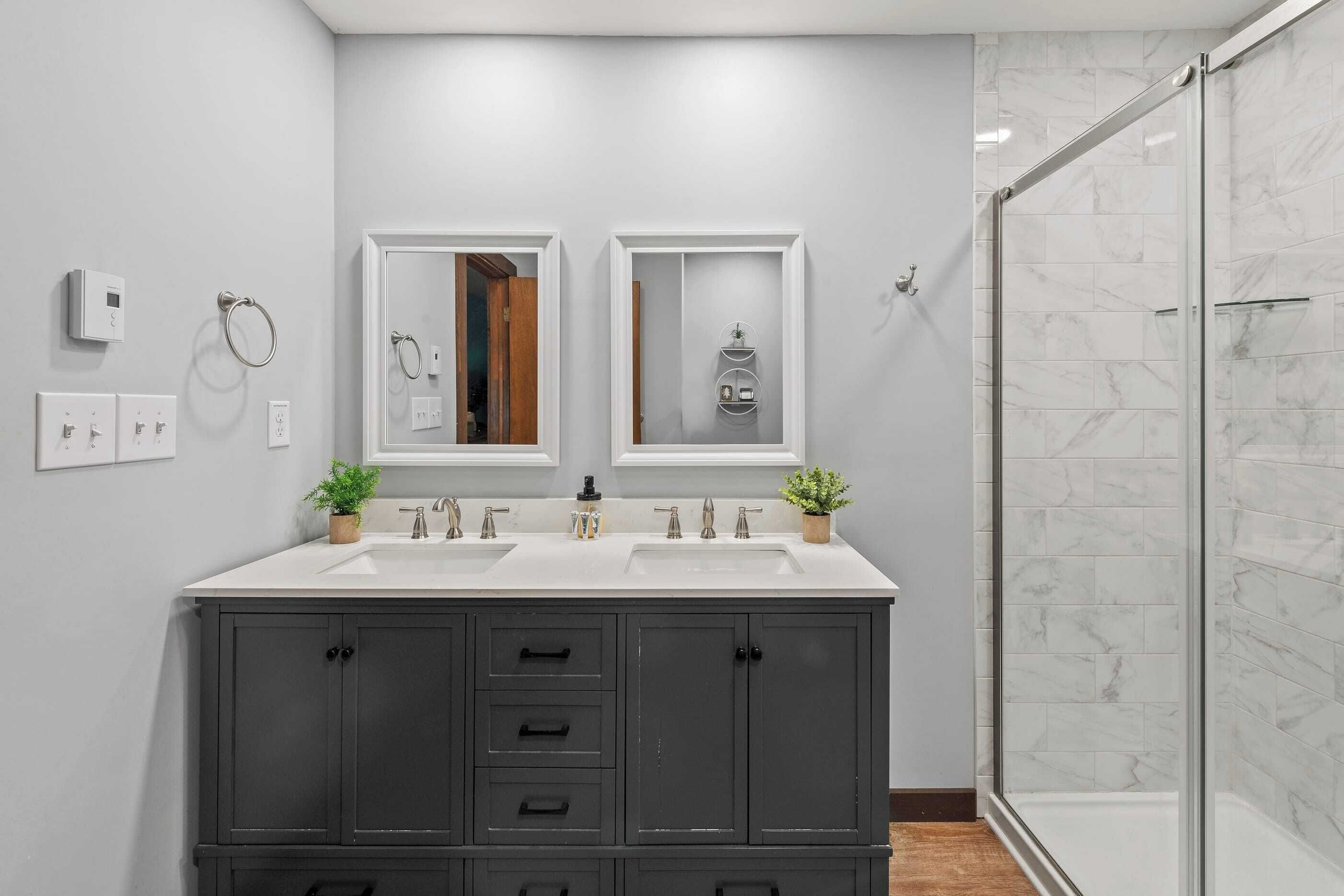 A modern bathroom with a double sink vanity, a glass shower enclosure, and a mirror with a wooden frame.