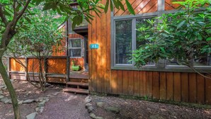 A wooden cabin with a 'WELCOME' sign, a number '63' sign, and a stone pathway leading to the entrance.