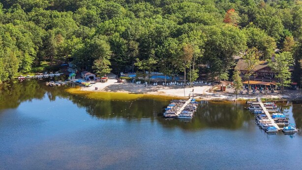 A lakeside resort with docked boats, a sandy beach, and a forested area. - The Boulder Inn by Avantstay Indoor Hot Tub, Game Room, Outdoor Fire Pit (Lake Harmony)