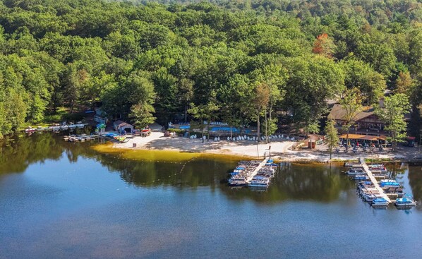 A lakeside resort with docked boats, a sandy beach, and a forested area.