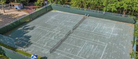 An outdoor tennis court surrounded by a green fence, with trees in the background.