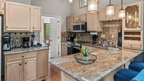 A modern kitchen with light wood cabinets, granite countertops, stainless steel appliances, and blue bar stools. - The Boulder Inn by Avantstay Indoor Hot Tub, Game Room, Outdoor Fire Pit (Lake Harmony)