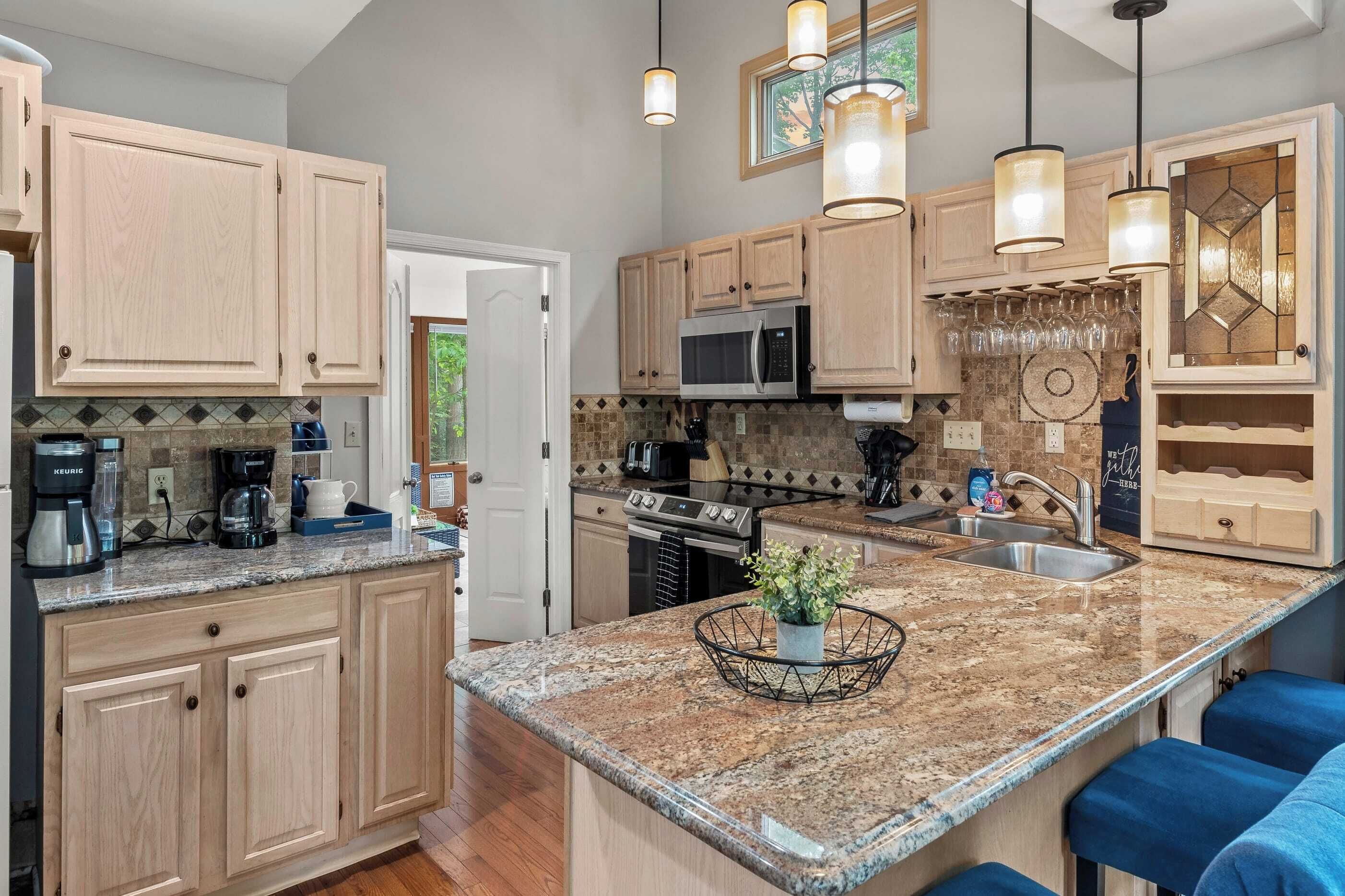 A modern kitchen with light wood cabinets, granite countertops, stainless steel appliances, and blue bar stools. - The Boulder Inn by Avantstay Indoor Hot Tub, Game Room, Outdoor Fire Pit (Lake Harmony)