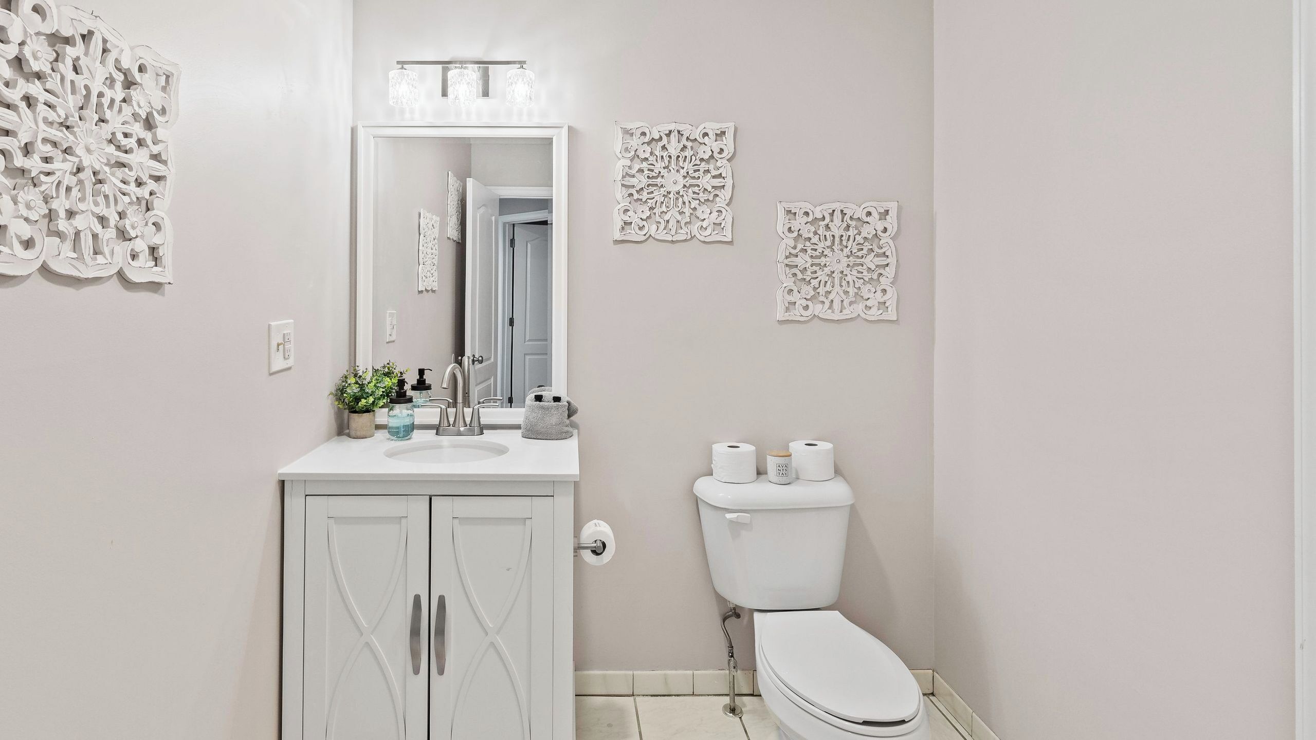 Une salle de bain avec un meuble-lavabo blanc, un miroir, des toilettes et des éléments décoratifs sur les murs.