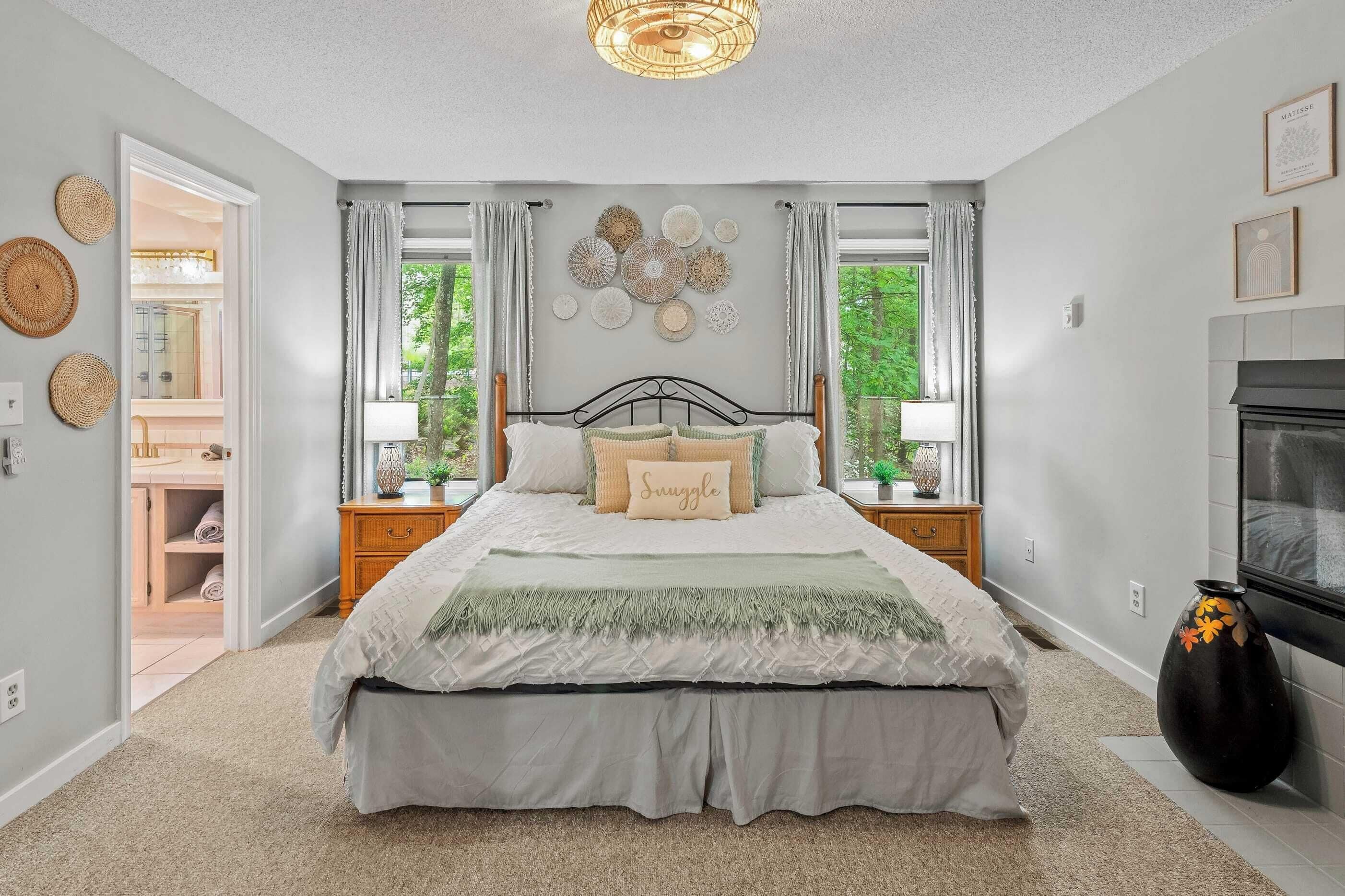 A bedroom with a large bed, a nightstand, a vase, and a fireplace.