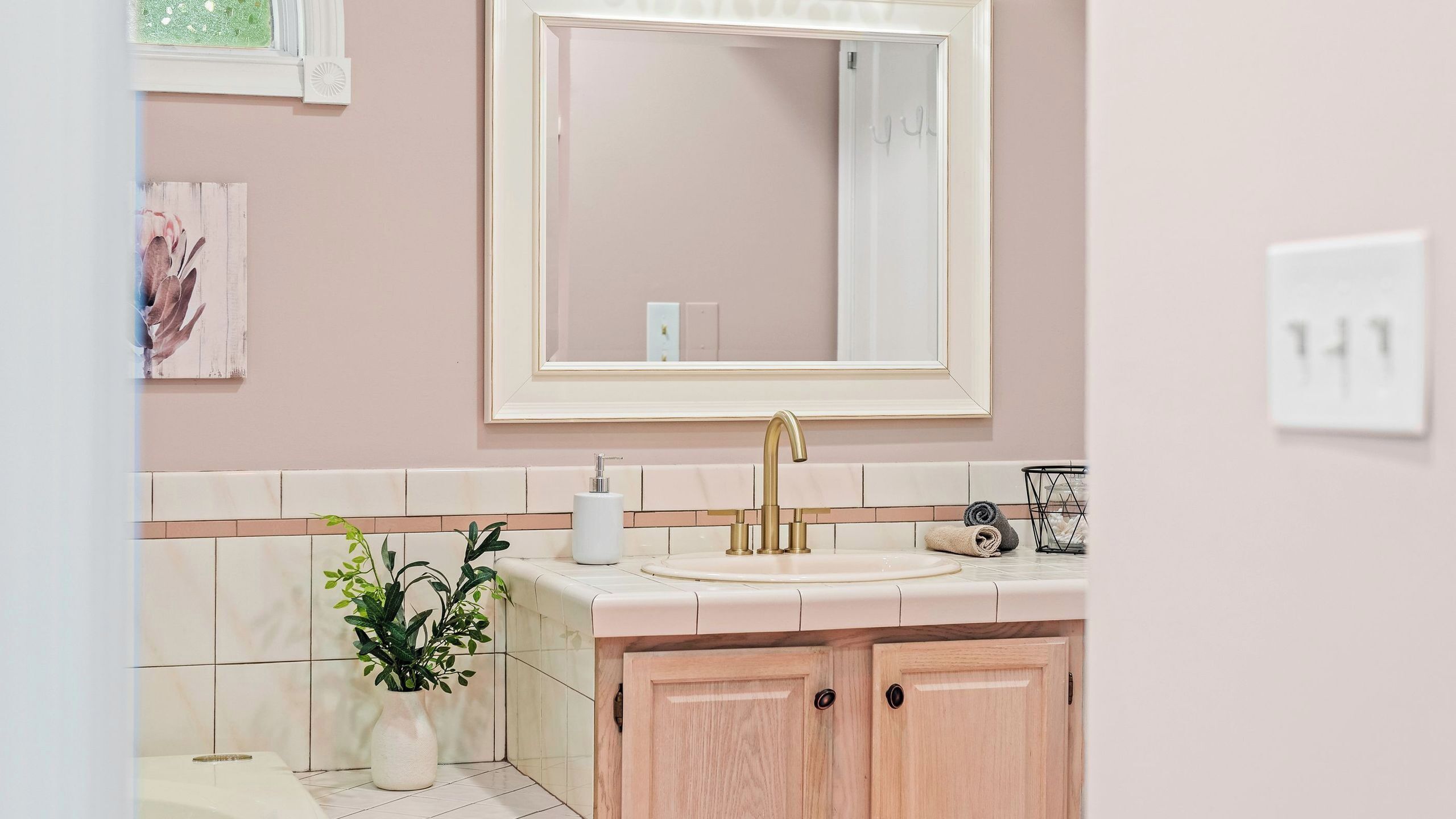 A bathroom with a large mirror, a sink, a potted plant, and a towel rack.