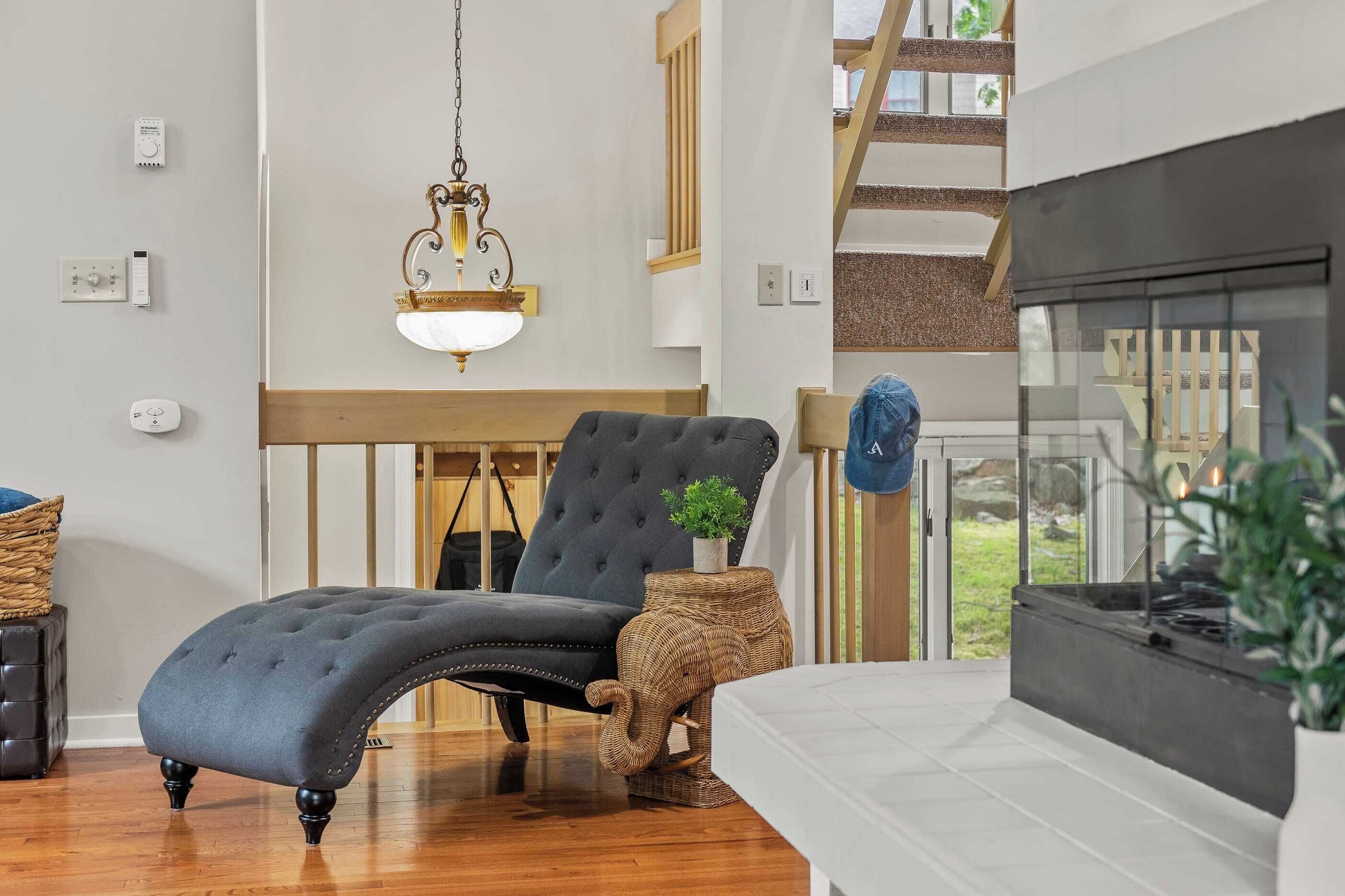 A modern living room with a black lounge chair, a fireplace, a hanging light fixture, and a view of the outdoors.
