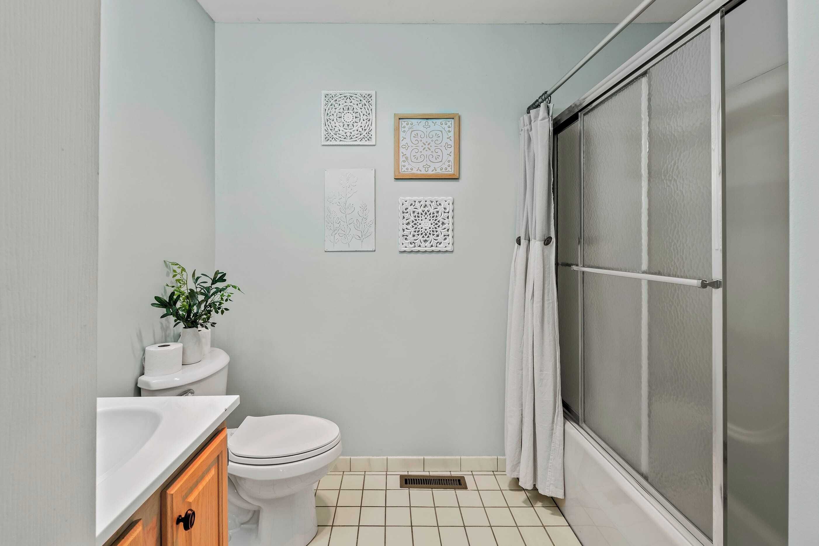 Une salle de bain équipée de toilettes, d’un lavabo et d’une douche. On y trouve également des éléments décoratifs muraux et une plante en pot.