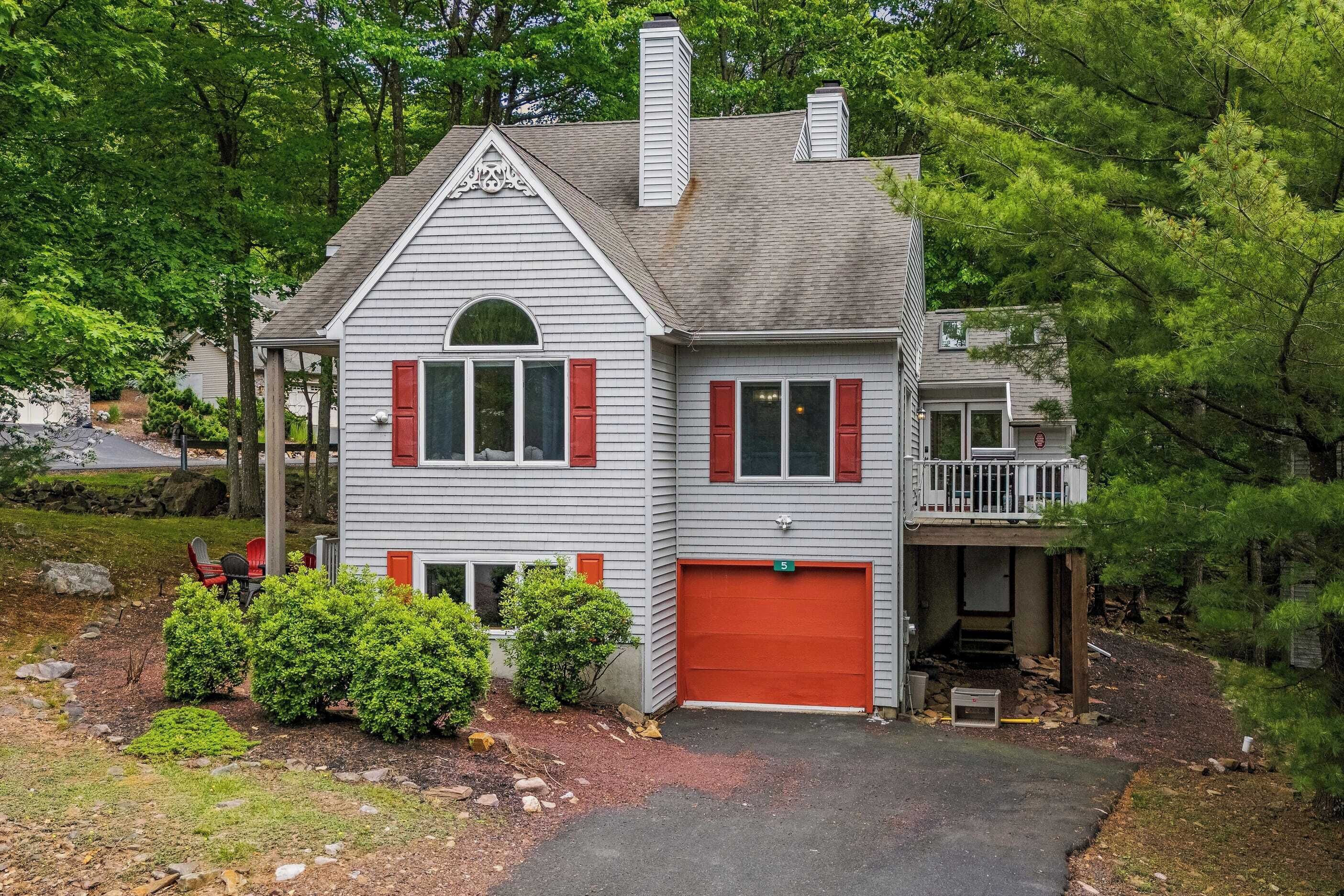 A two-story house with a red garage door, a covered porch, and a small deck.