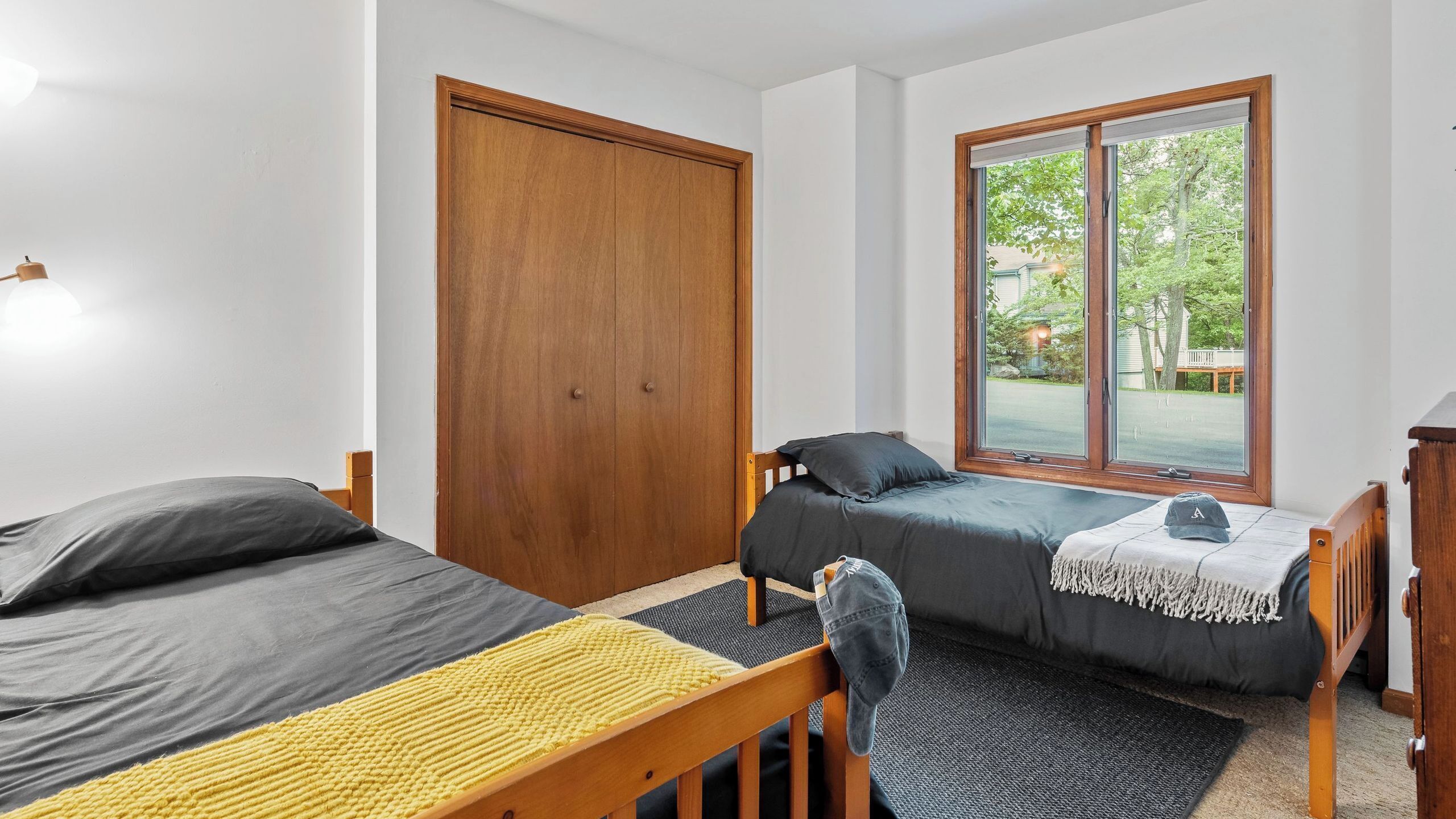 A room with two beds, a wooden wardrobe, a large window with a view, and a small desk.