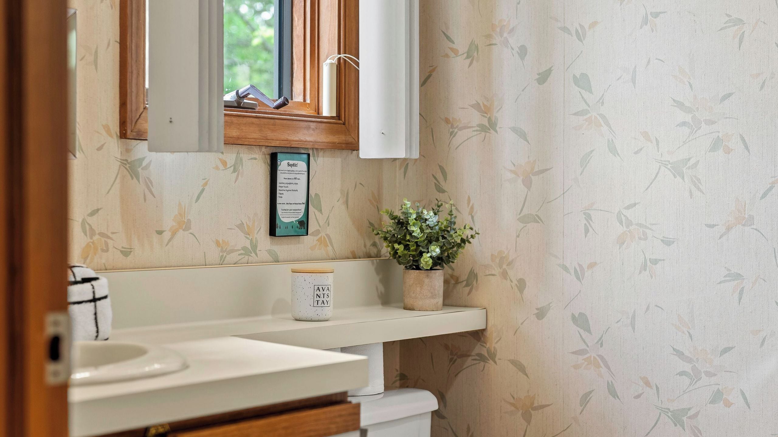 Een badkamer met een houten wastafelmeubel, een plant in pot en een bord aan de muur.