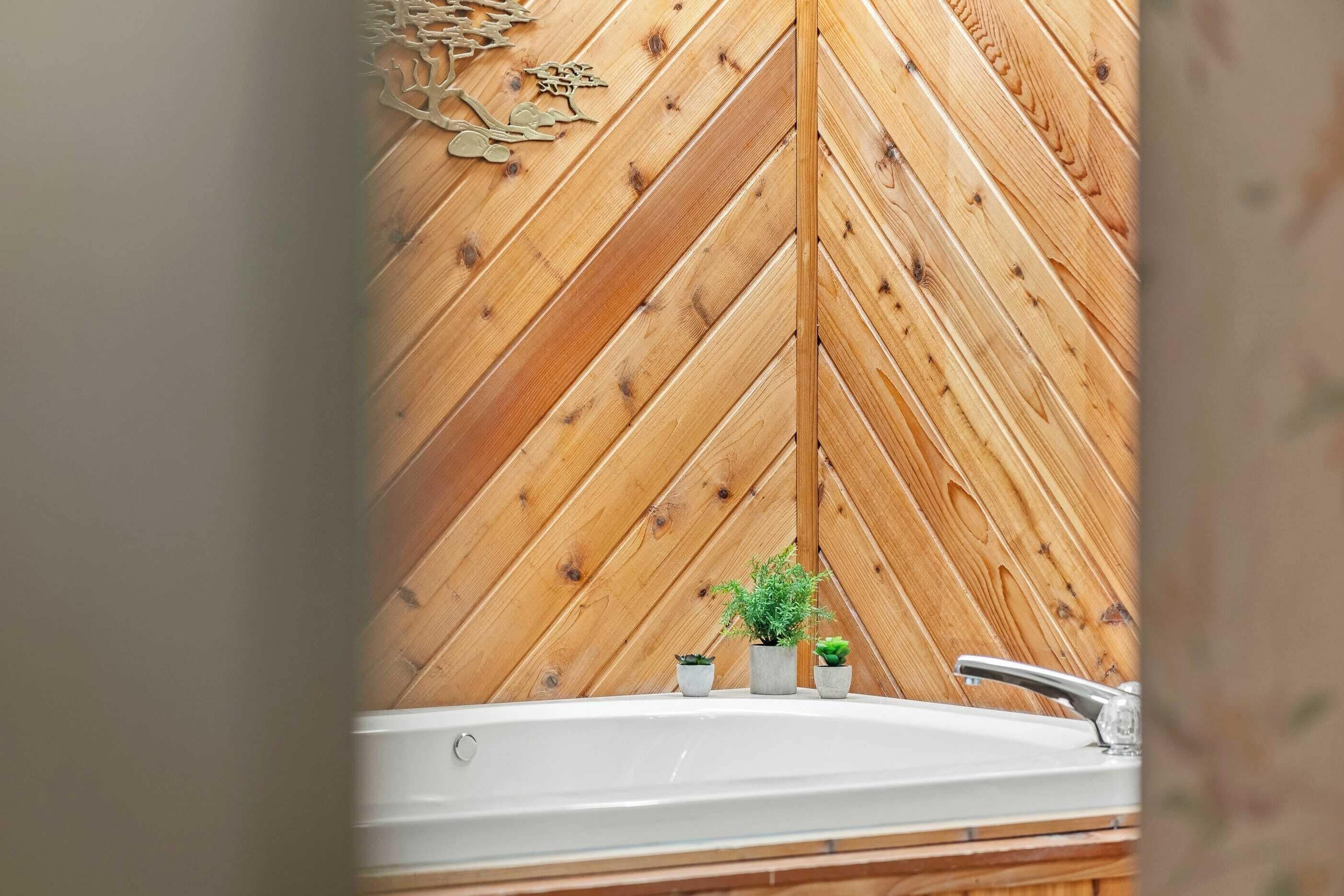 A bathroom with a wooden herringbone wall, a bathtub, and three small potted plants.