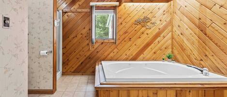 Un baño con paneles de madera, una bañera independiente, un ventanal y una puerta que da a otra habitación.