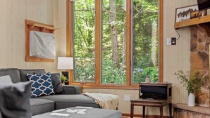 A cozy living room with a grey sofa, a small table, and a large window offering a view of trees. - Harmony Ridge by Avantstay Fireplace, Large Deck & Forest Views (Lake Harmony)