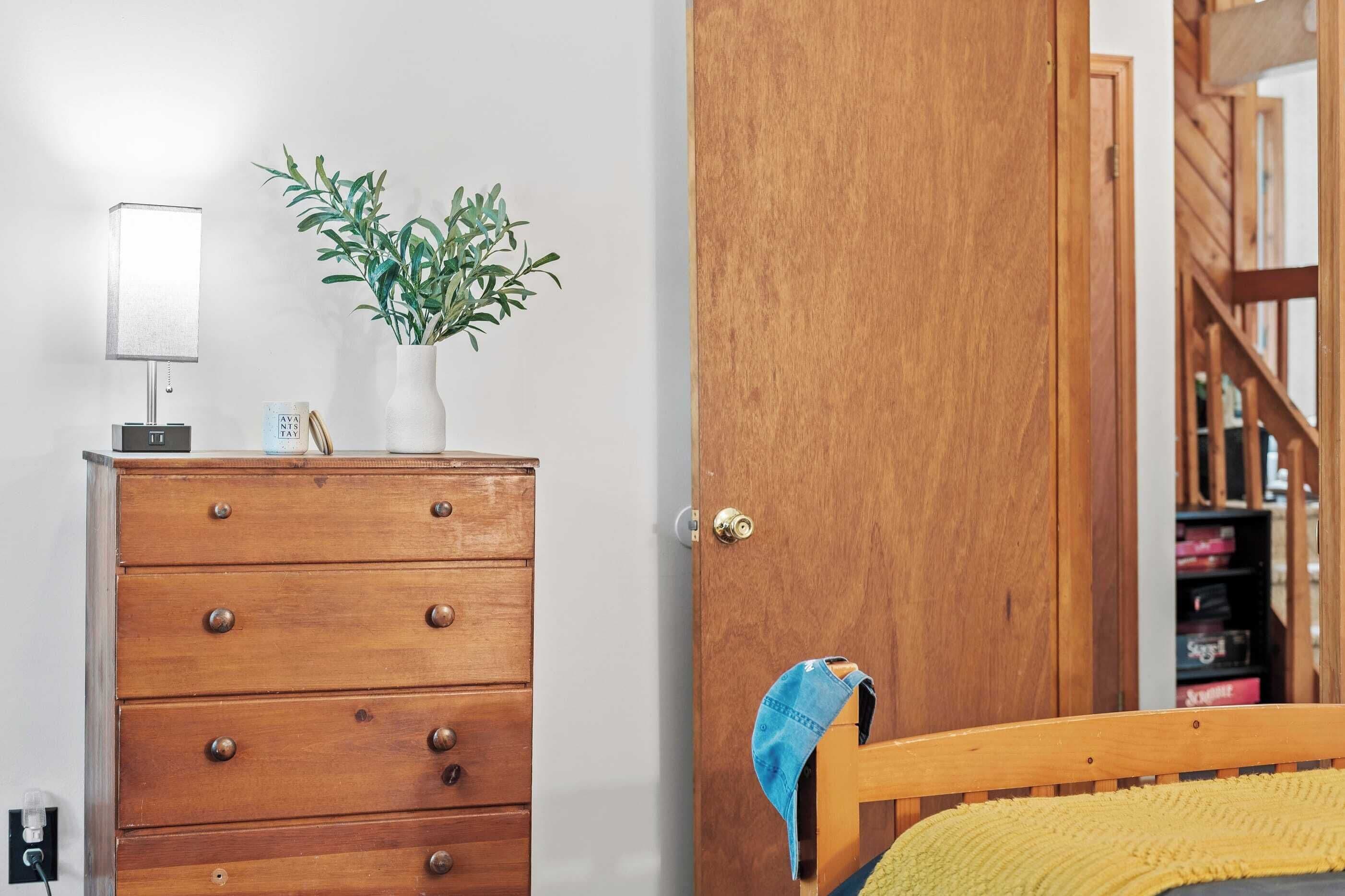 Une commode en bois avec des tiroirs, une lampe et une plante en pot.