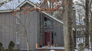 A two-story building with a dark gray exterior, a red door, and a number '69' sign. - Frost Hollow by Avantstay Deck w/ Grill, Game Room Loft (White Haven)