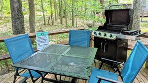 An outdoor grill area with a table and chairs, surrounded by trees. - Frost Hollow by Avantstay Deck w/ Grill, Game Room Loft (White Haven)