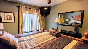 A hotel room with a bed, a television, a mirror, a lamp, and a window with curtains.