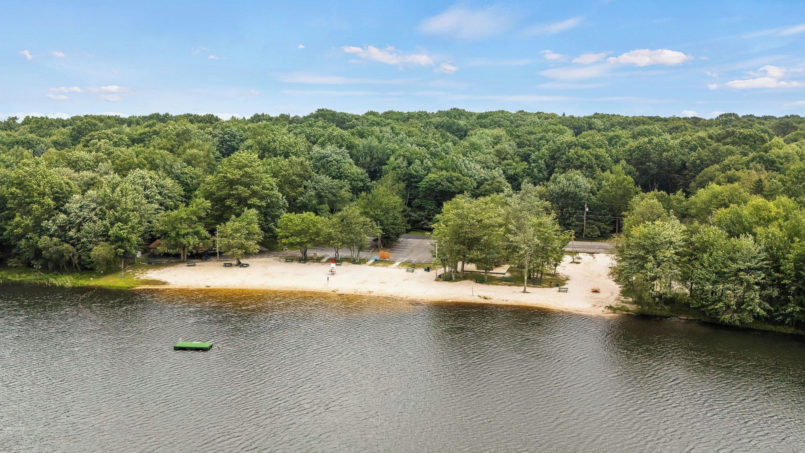 Un parque junto al lago con áreas de picnic, un muelle para embarcaciones y un bosque denso al fondo.