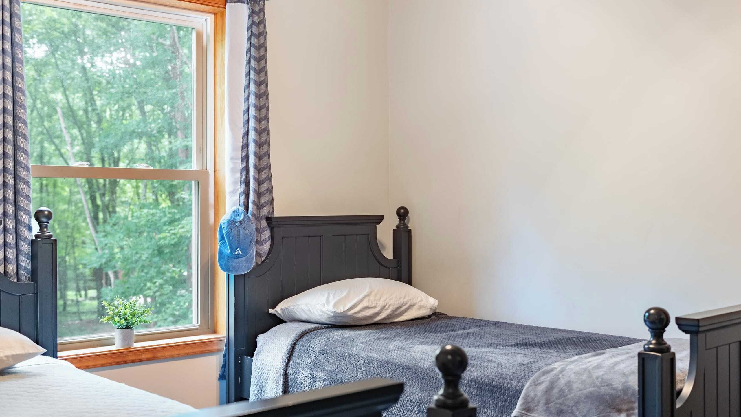 Un dormitorio con cama, ventana con cortinas y vista a árboles desde afuera.