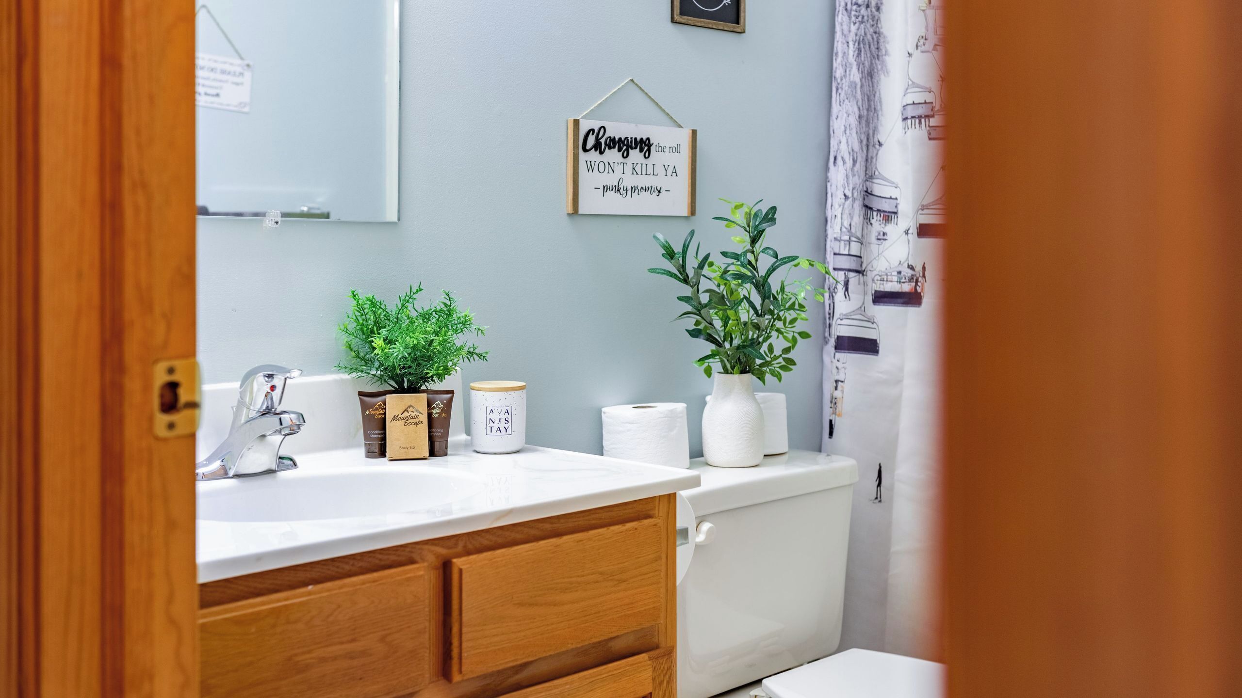 Ein Badezimmer mit einem weißen Waschbecken, Holzschränken, einem Spiegel, einem Handtuchhalter und einem Schild an der Wand.