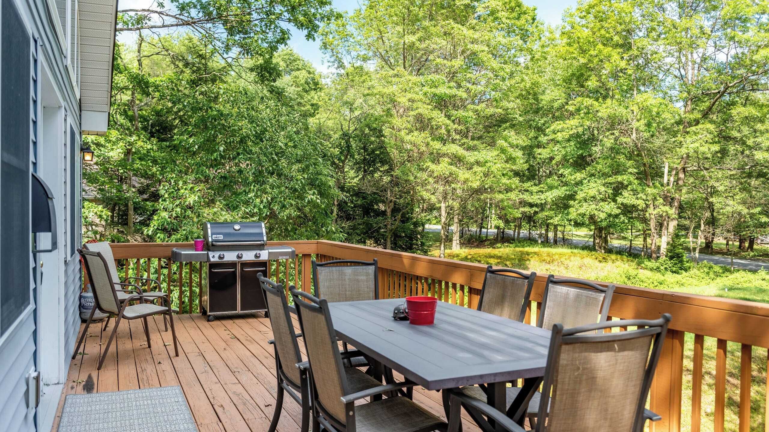 An outdoor deck with a grill, dining table, and chairs.