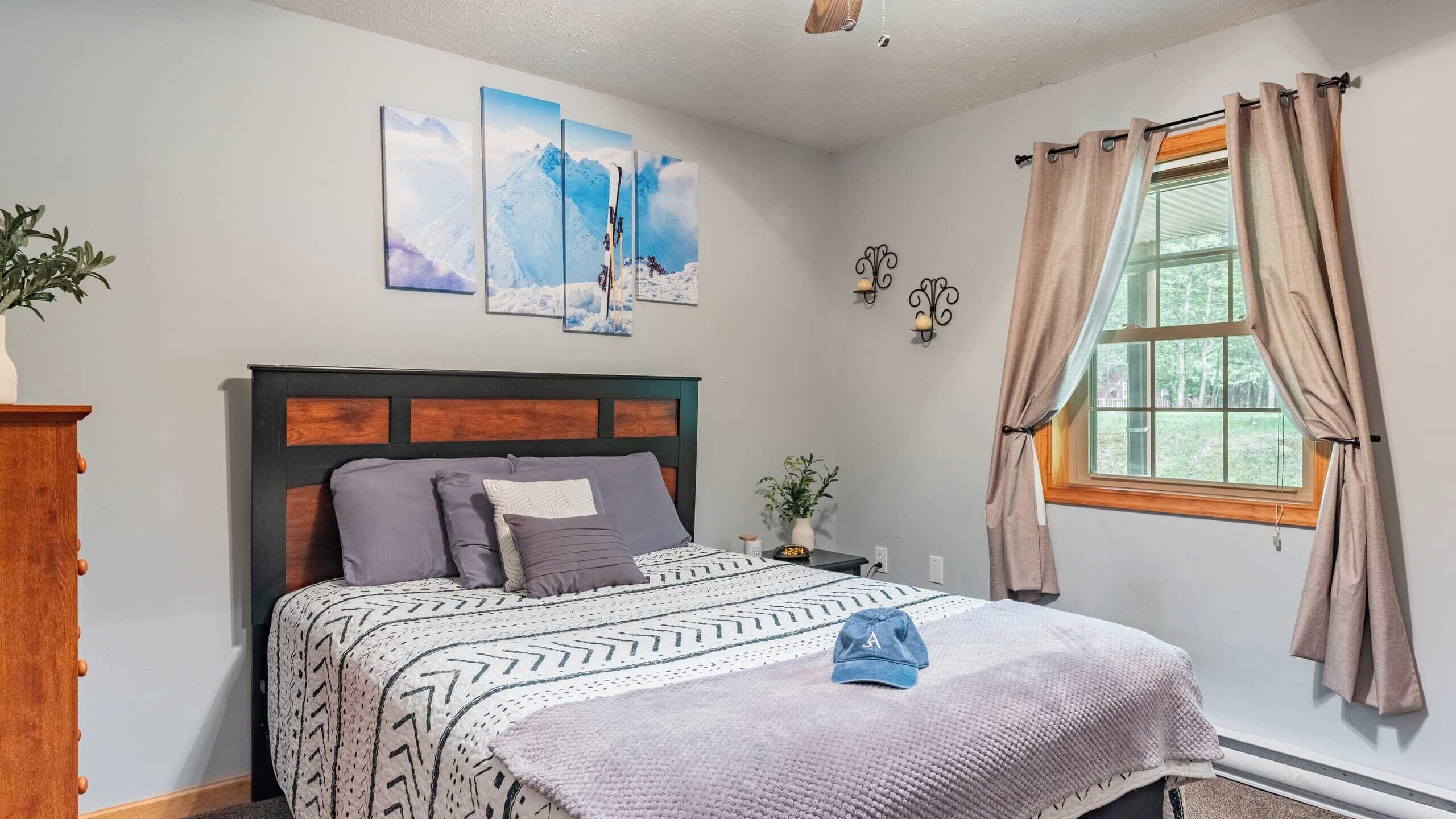 A bedroom with a bed, a nightstand, a clock, a window with curtains, and wall art.