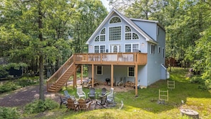 A two-story house with a wooden deck and a covered porch, surrounded by trees. - The Nest at Brier Crest by Avantstay Game Room, Expansive Deck & Fire Pit (Blakeslee)