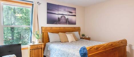 A bedroom with a wooden bed, a nightstand, a desk with a chair, and a window with curtains.