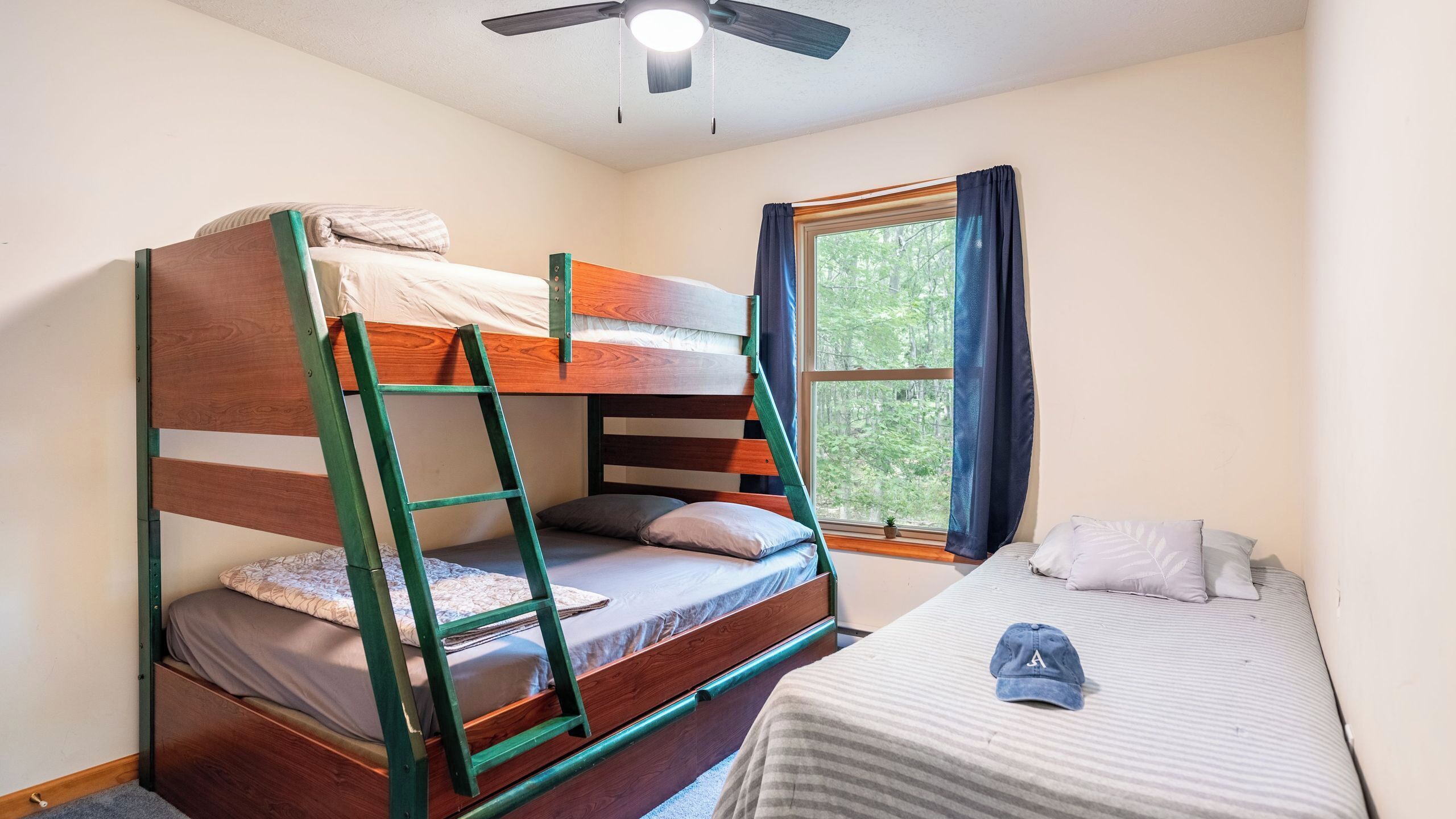 Habitación con literas, una escalera, una ventana con cortinas y un ventilador de techo.