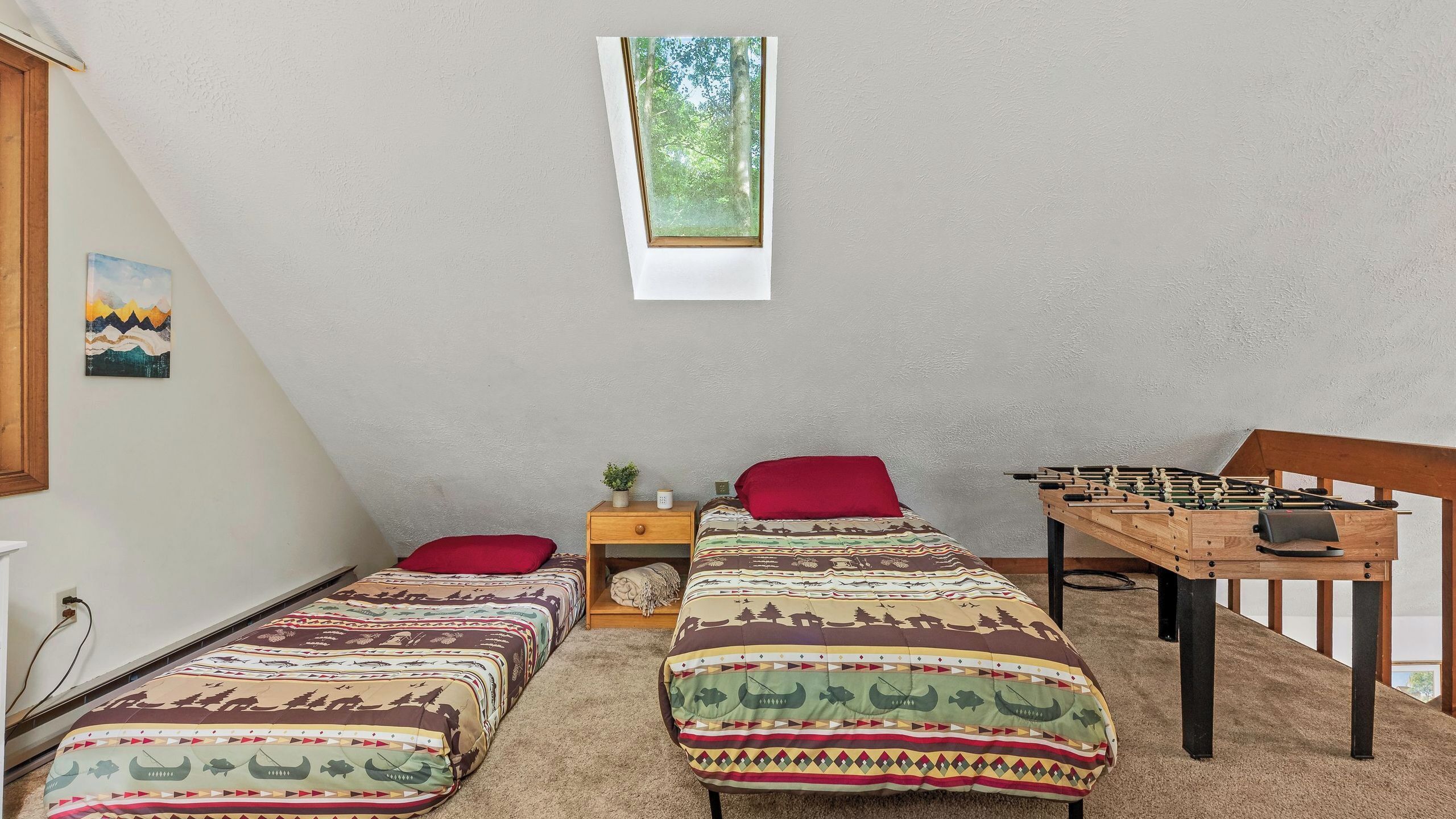 Une chambre avec deux lits, une fenêtre, une petite table avec une plante et une table de baby-foot.