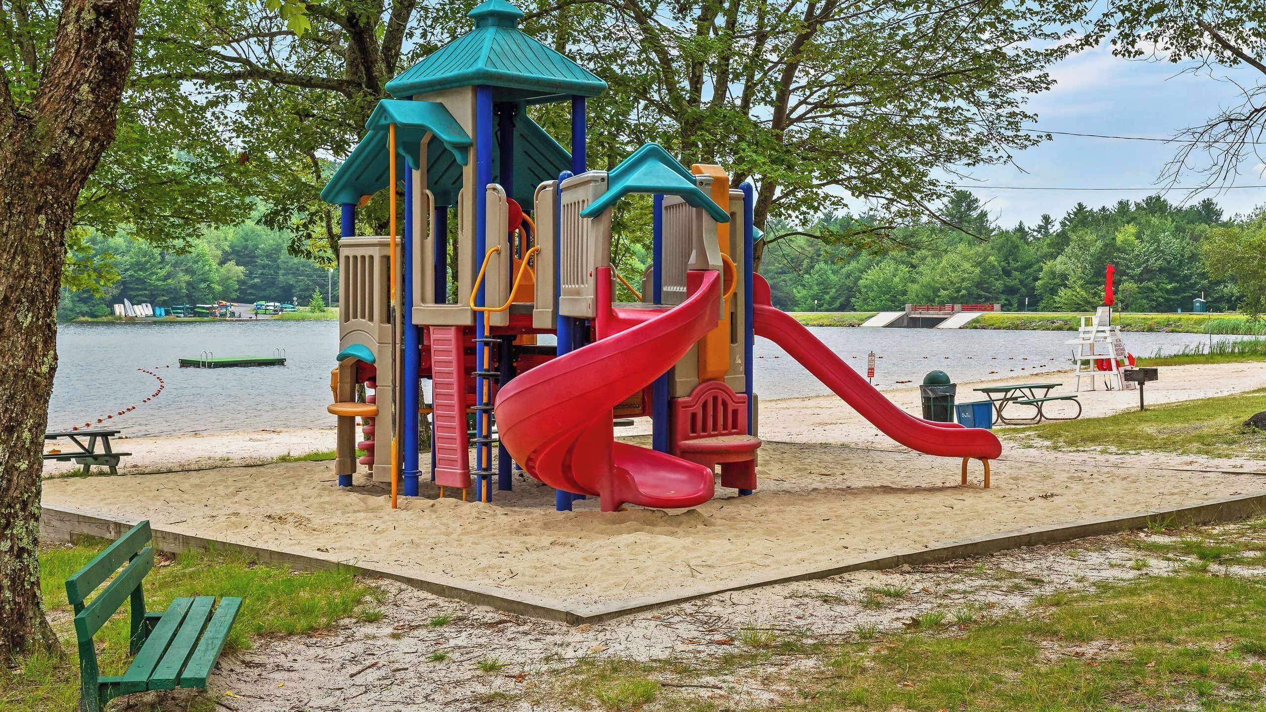 A playground with a red slide and a climbing structure near a lake.