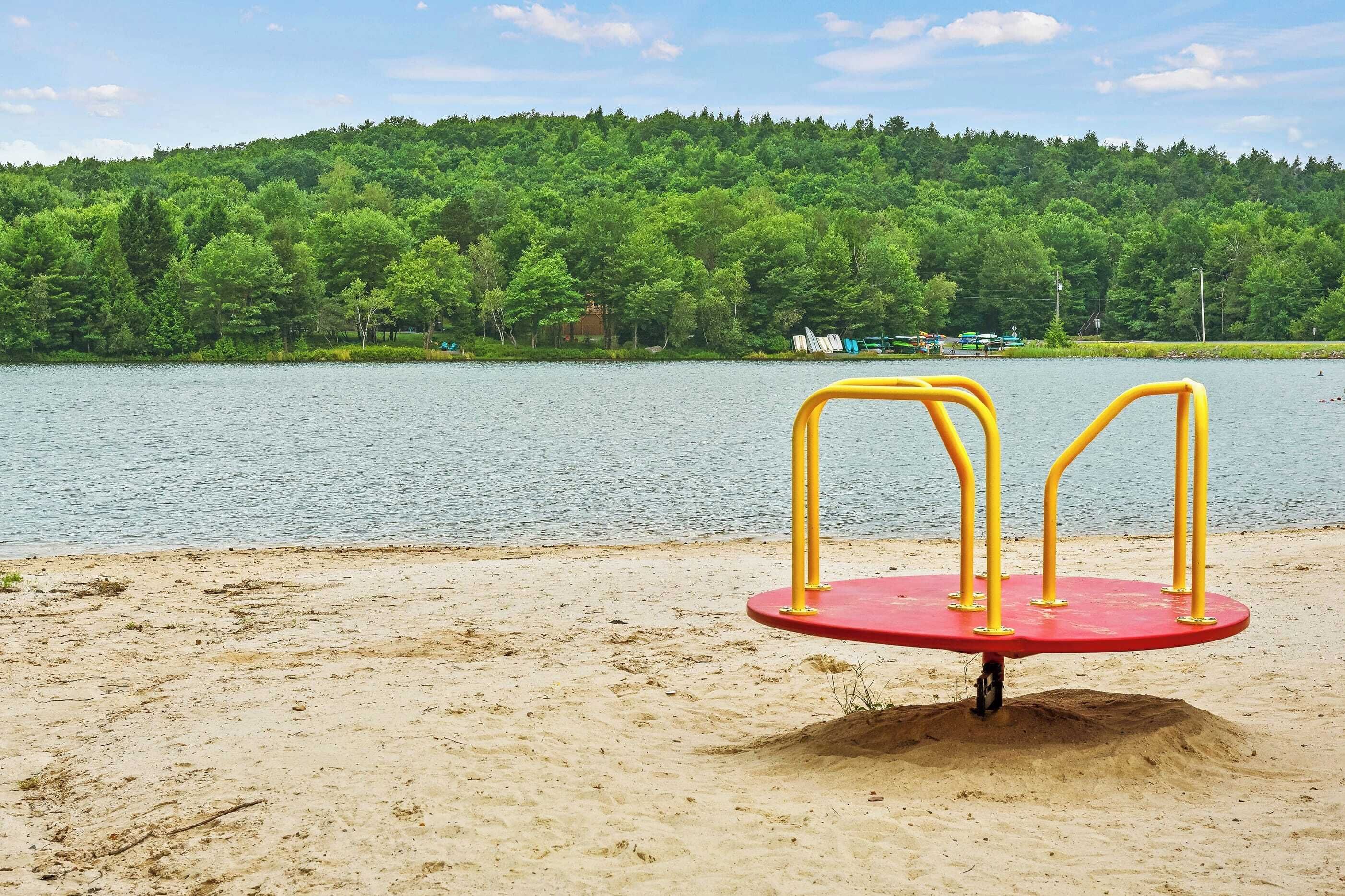 A playground with yellow and red equipment near a lake with a forested hill in the background.