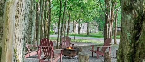 A campsite with a fire pit and Adirondack chairs.