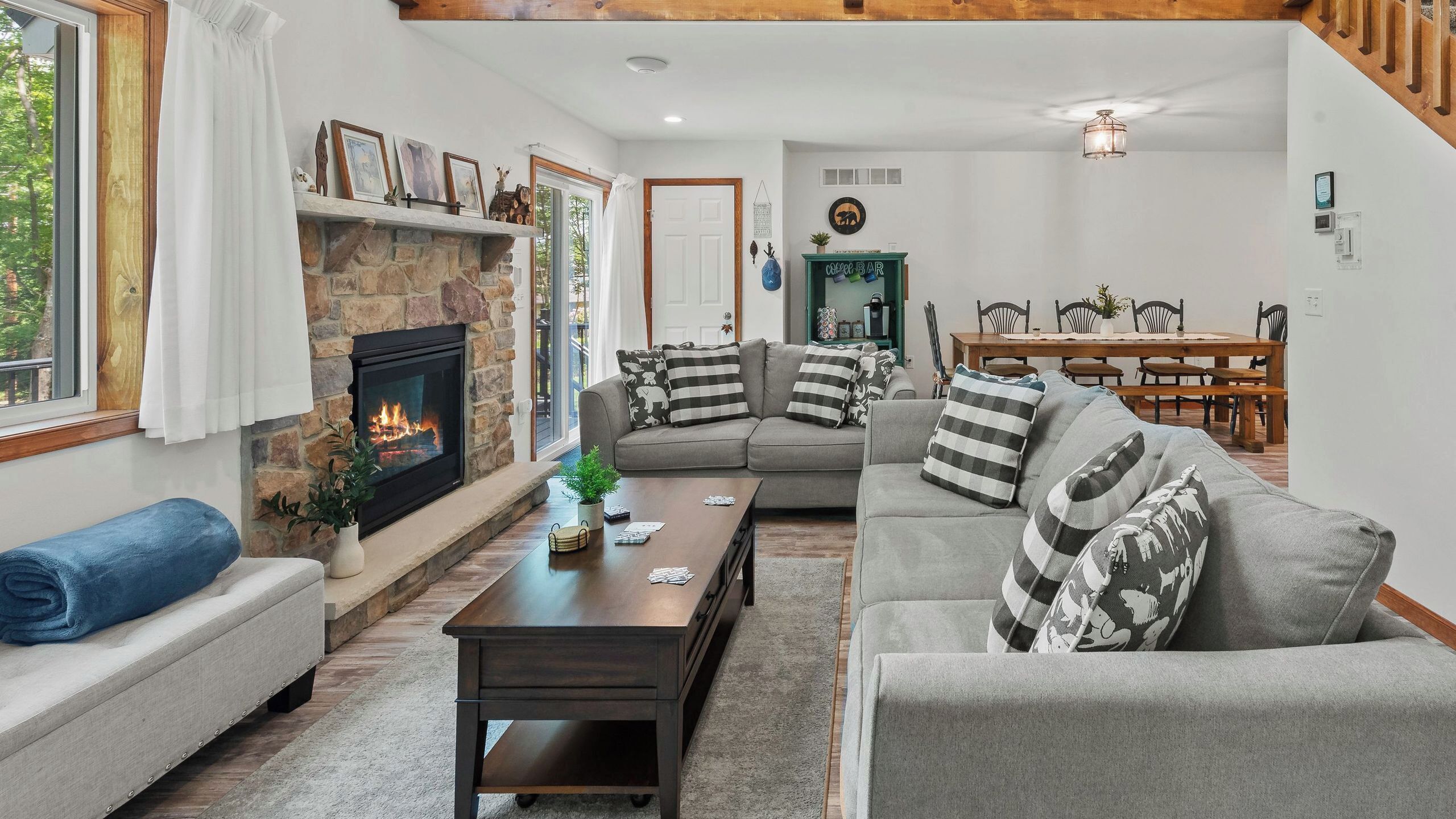Una sala de estar con chimenea de piedra, un sofá gris, una mesa de centro de madera y un comedor con una mesa y sillas de madera.