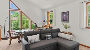 Una sala moderna con un sofá modular, una mesa de comedor y vistas a un bosque a través de amplios ventanales.