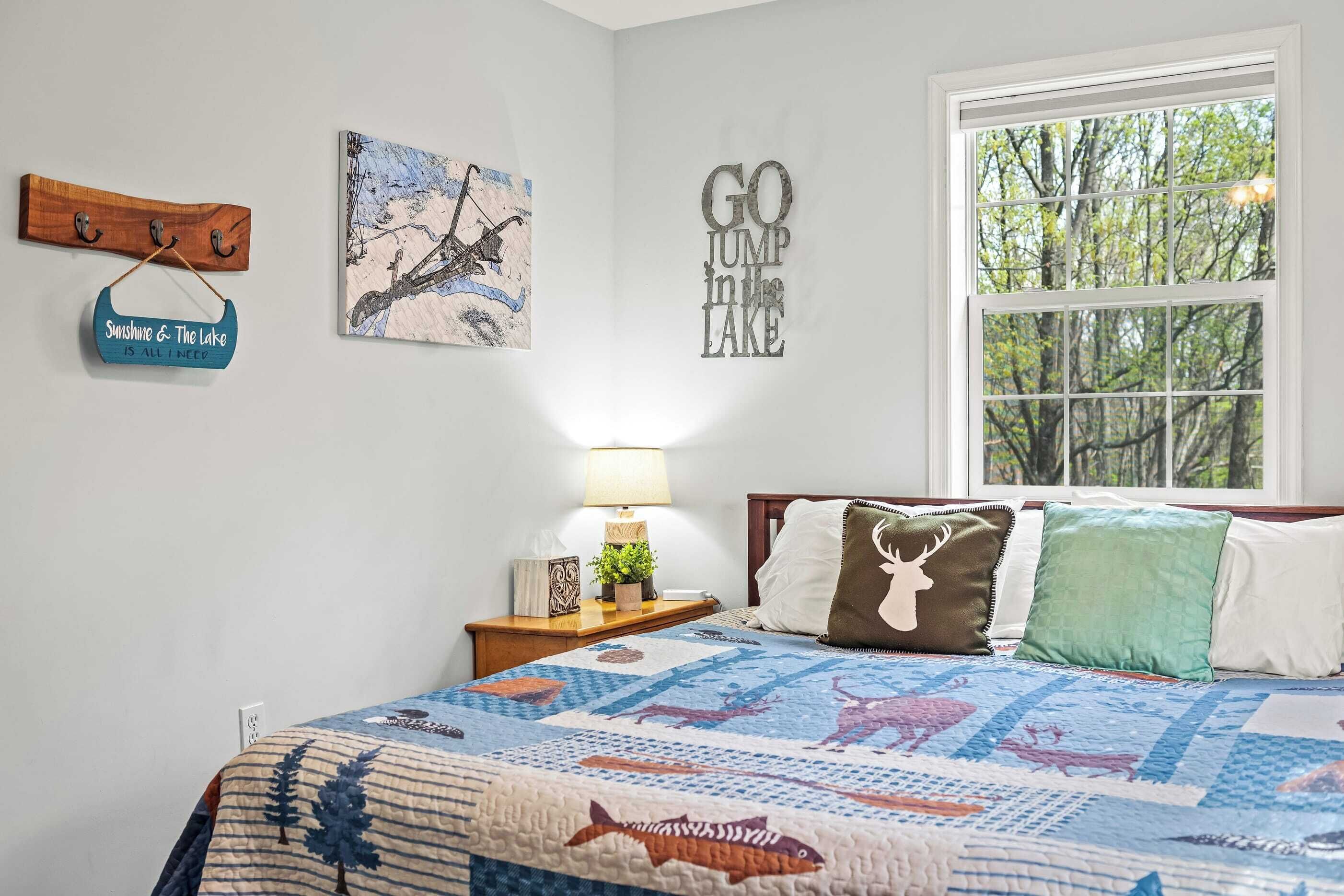 A bedroom with a bed, a nightstand, a window, and wall decorations including a sign and a painting.