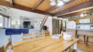 A cozy cabin interior with a stone fireplace, wooden dining table, and kitchen area. - Chalet All Day Avantstay Lakeside, Firepit, Shared Pool (Pocono Lake)