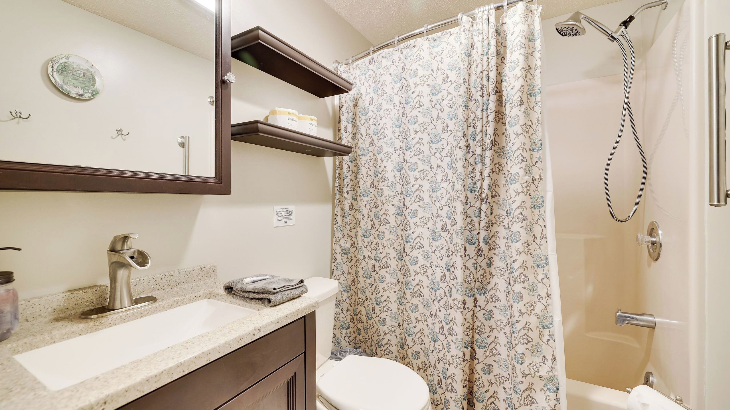 A bathroom with a shower, toilet, sink, and a mirror with a shelf above it.