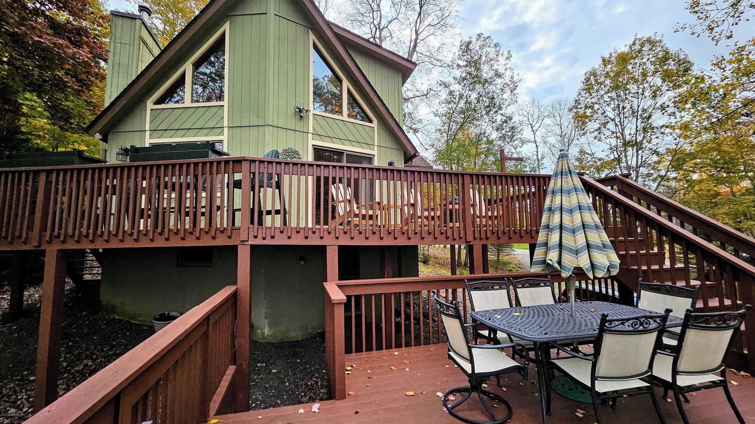 A two-story house with a deck, outdoor furniture, and a staircase.