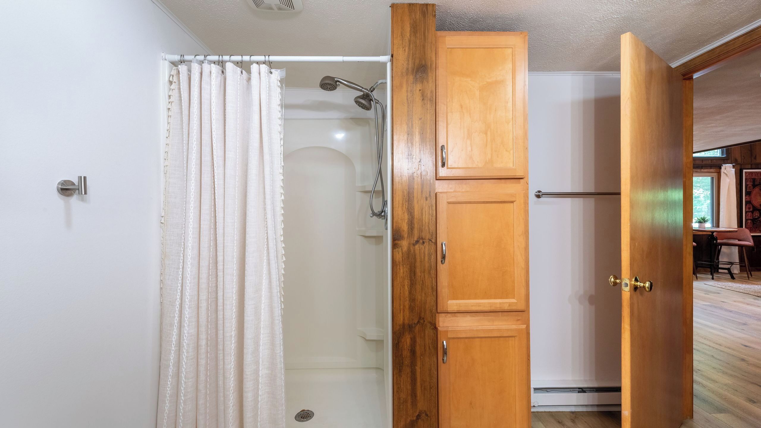 A bathroom with a shower, a wooden door, and a white curtain.