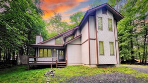 A modern two-story cabin with large windows, a deck, and a natural forest setting.