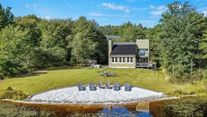 A modern house with a deck, surrounded by a grassy yard and a pond.