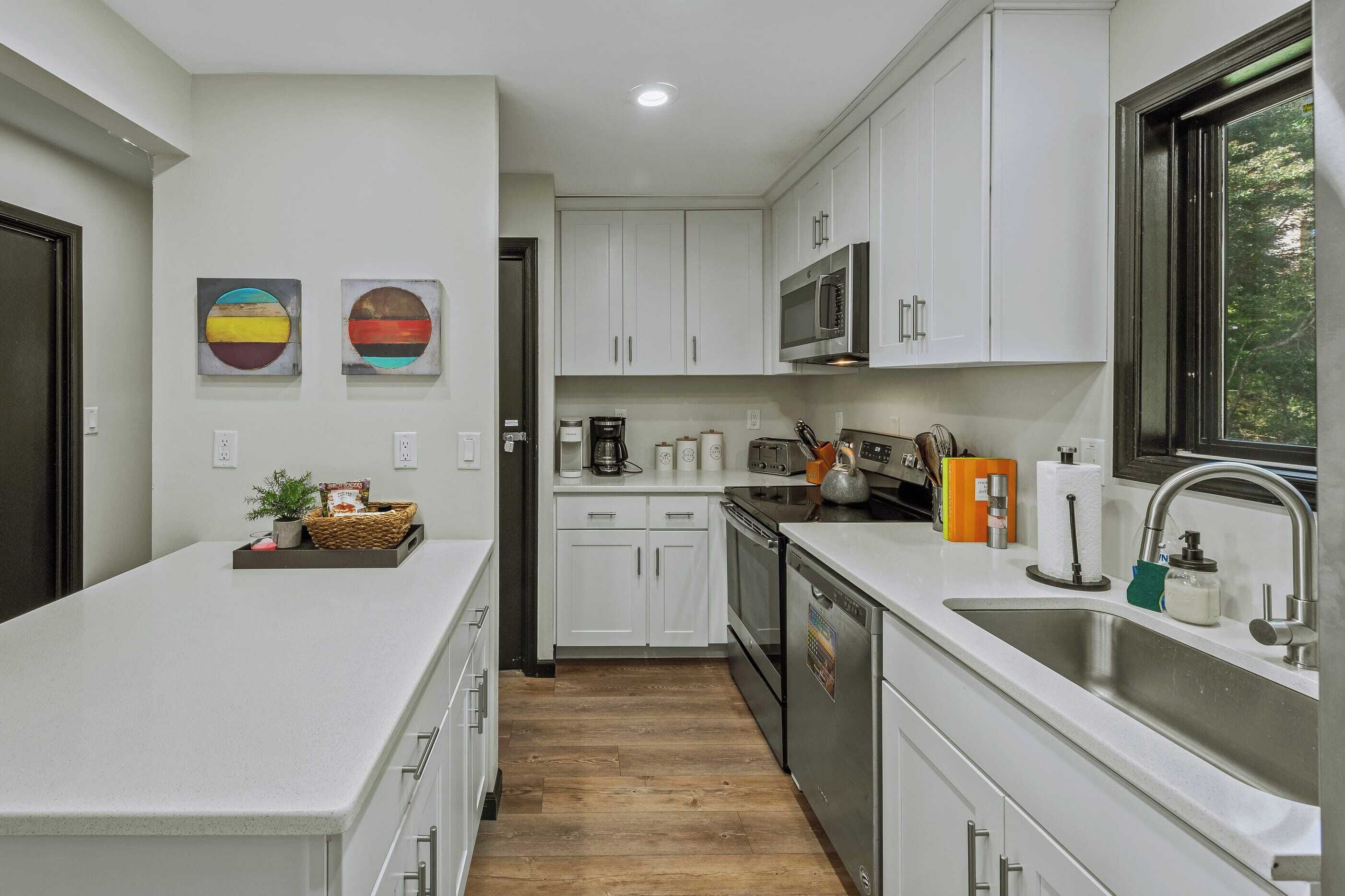 A modern kitchen with white cabinets, stainless steel appliances, and a wooden floor.