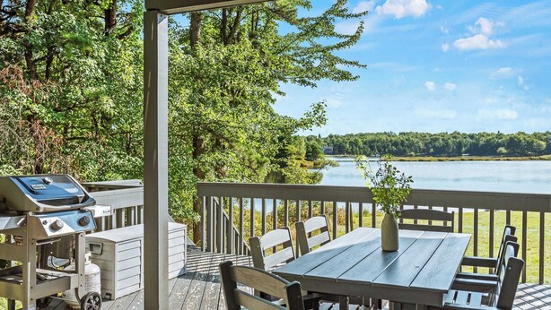 A wooden deck with a table and chairs, overlooking a lake.