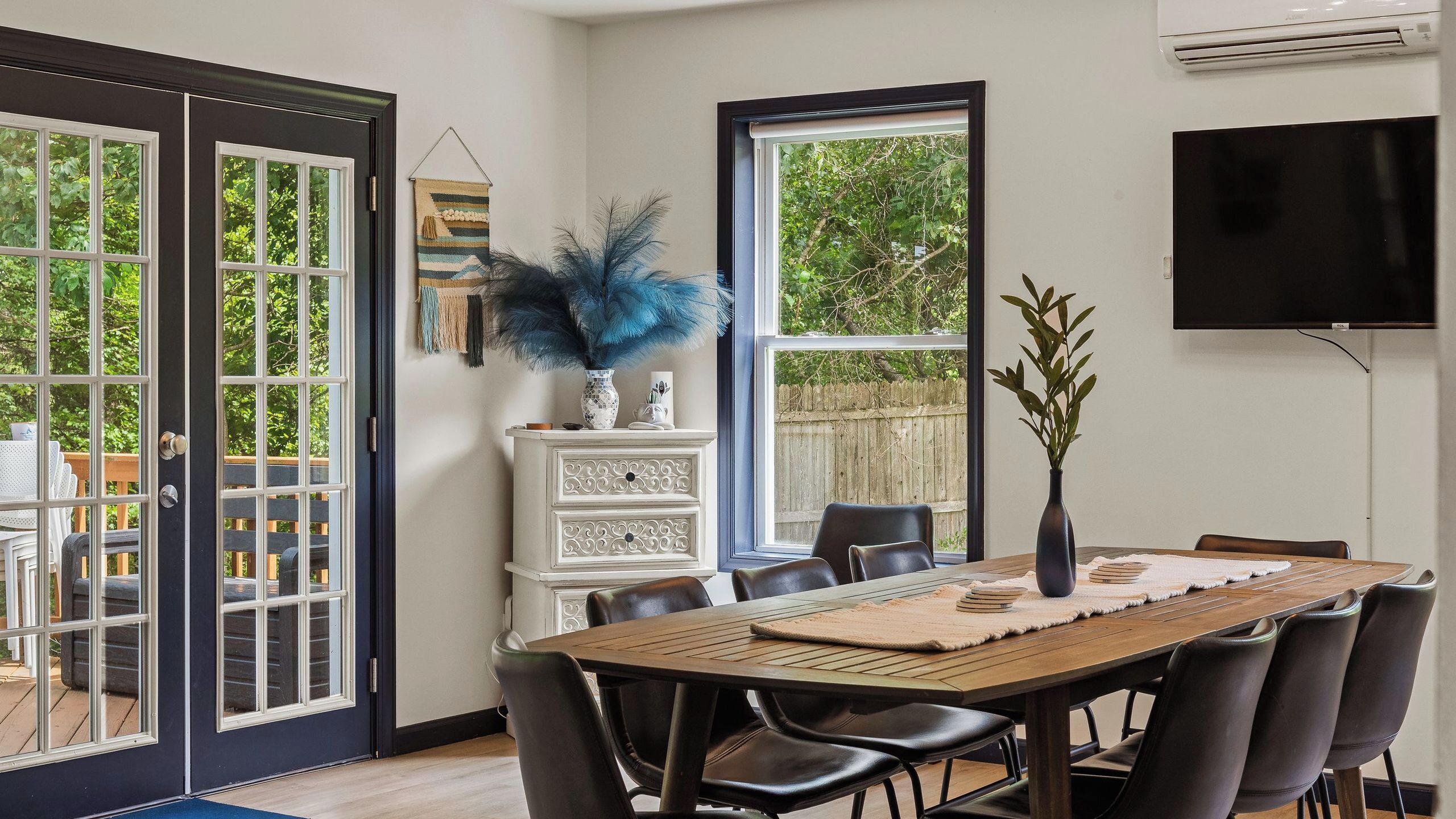 A dining area with a wooden table, black chairs, a white cabinet, and a large window with a view of greenery.