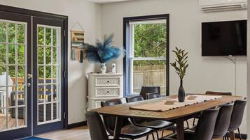 A dining area with a wooden table, black chairs, a white cabinet, and a large window with a view of greenery.