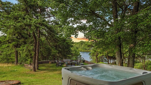 Ein Whirlpool, umgeben von einer Terrasse mit Blick auf einen See, Bäume und einen Holzzaun.