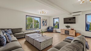 Ein modernes Wohnzimmer mit Ecksofa, Couchtisch, Fernseher und großen Fenstern.